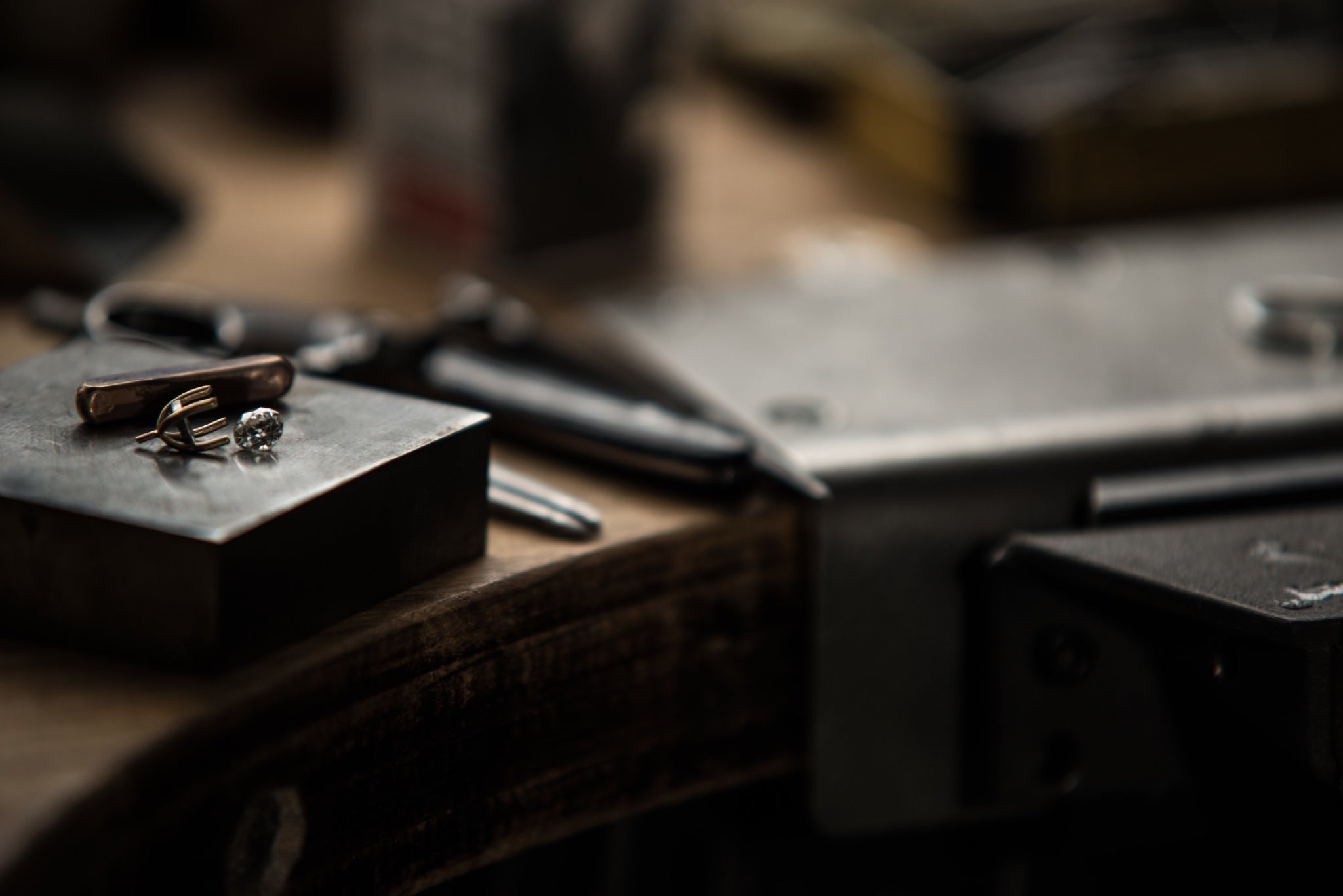 Dark moody shot of a jeweller's workbench, with a loose diamond and setting on top of it