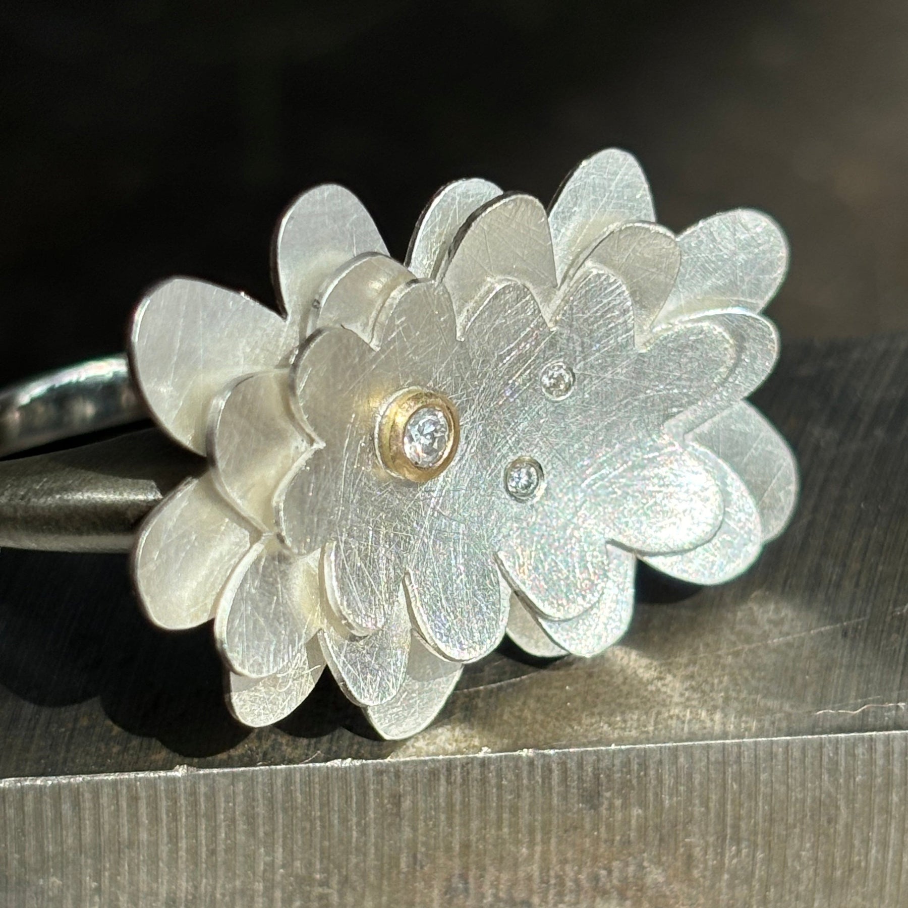 sterling silver abstract flower ring with three diamonds, one set in gold, on a steel background