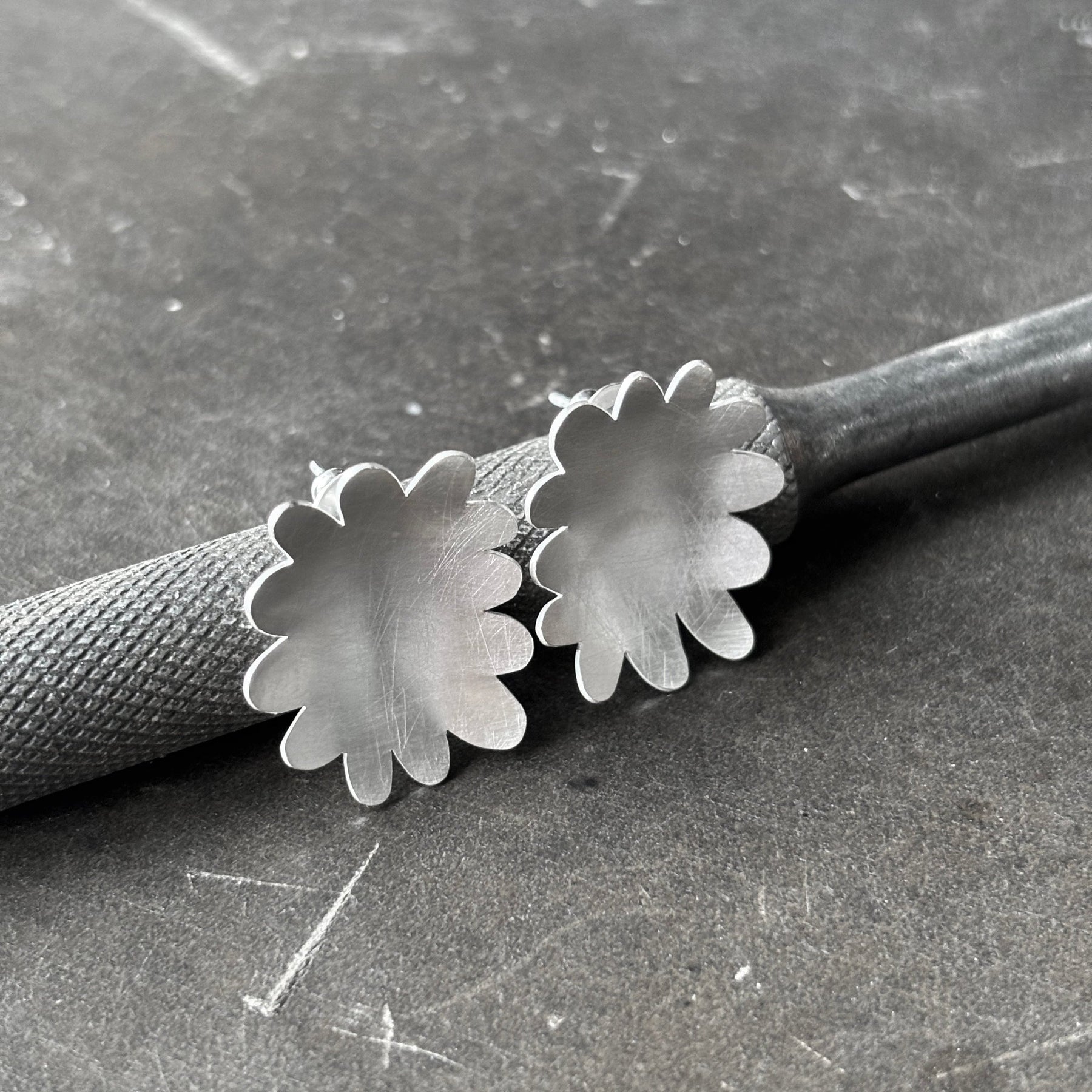 Large sterling silver flower abstract studs leaning on steel tool