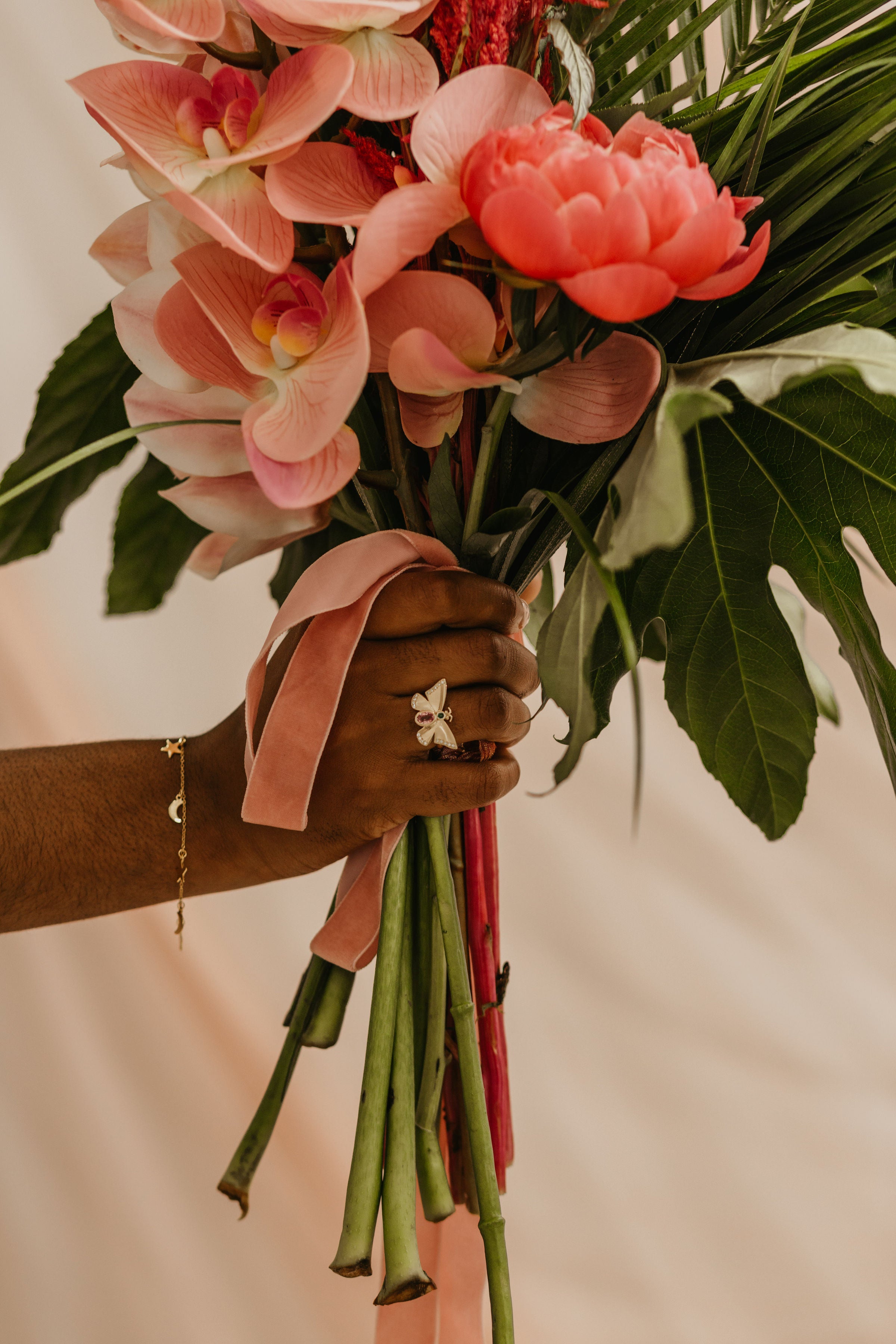 Woman holding a bunch of pink flowers, wearing a bespoke gold butterfly ring