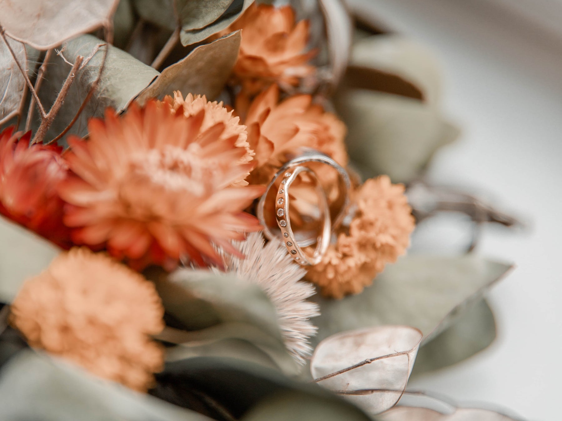 Two handmande bespoke white gold wedding rings set with diamonds, resting on an orange flower