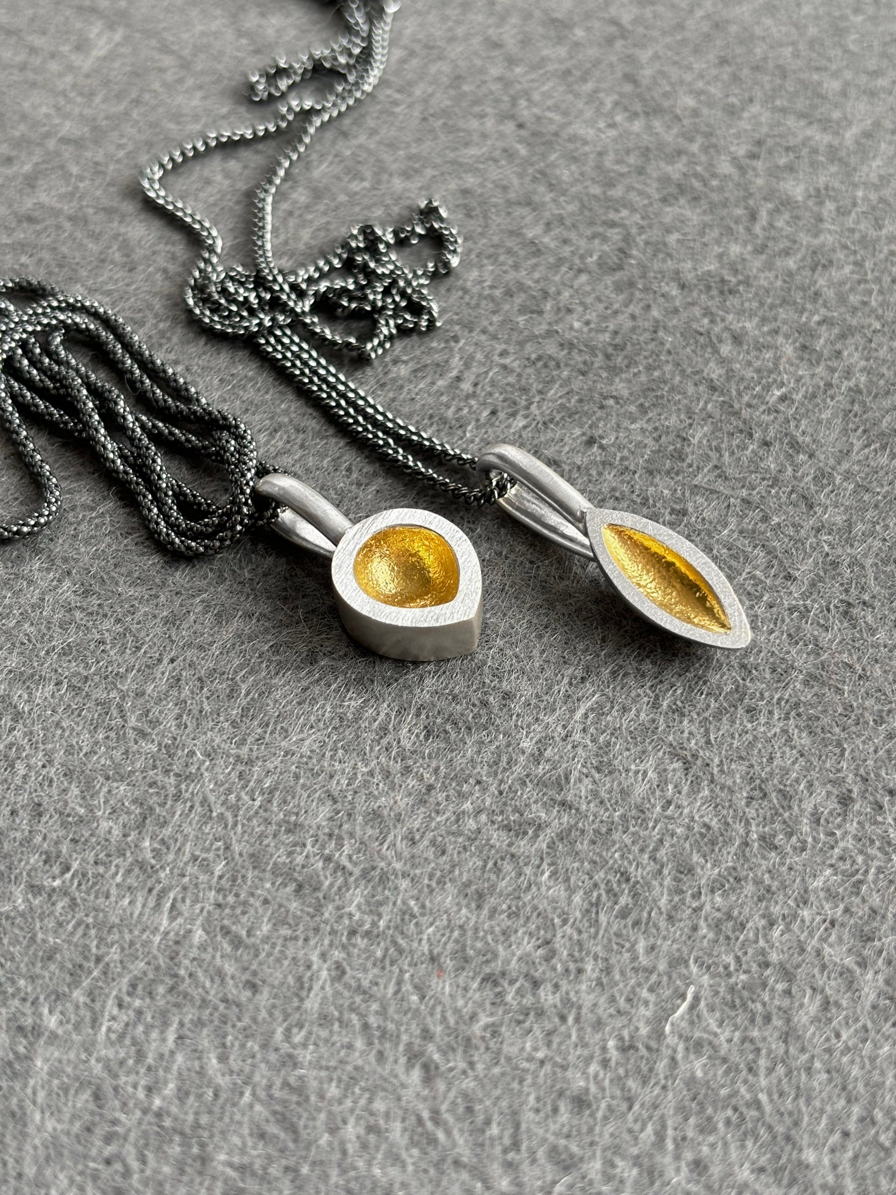 Silver seed pod shaped pendants with oxidised chains on a grey background
