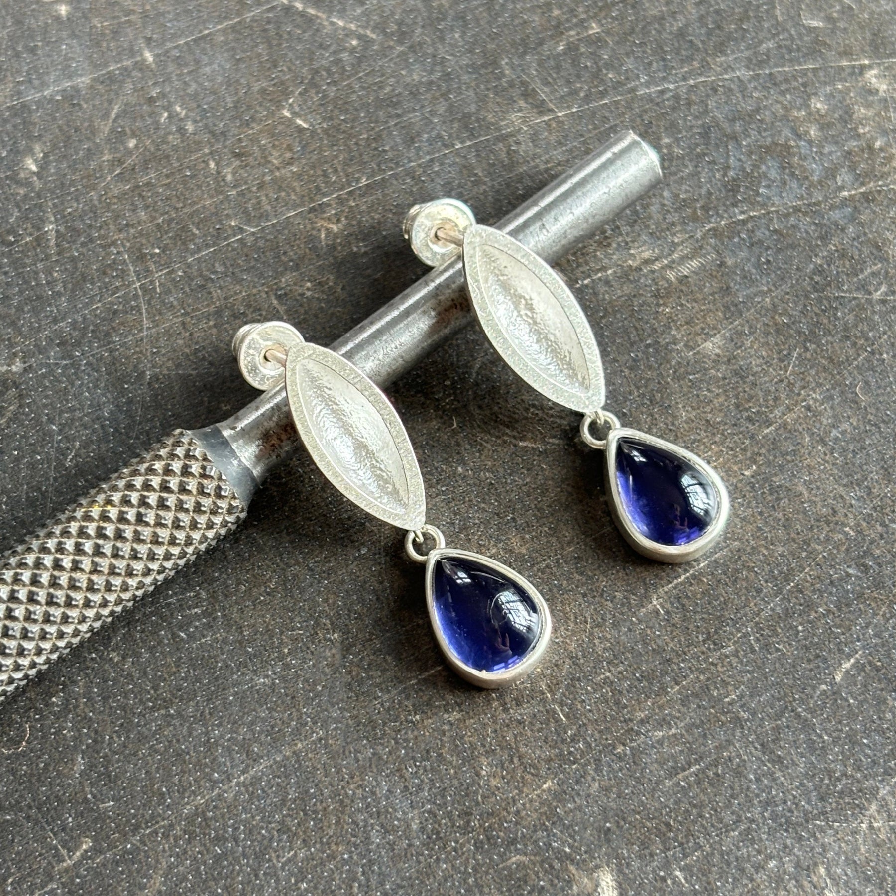 sterling silver sand cast earrings wth iolite stone leaning on a steel tool