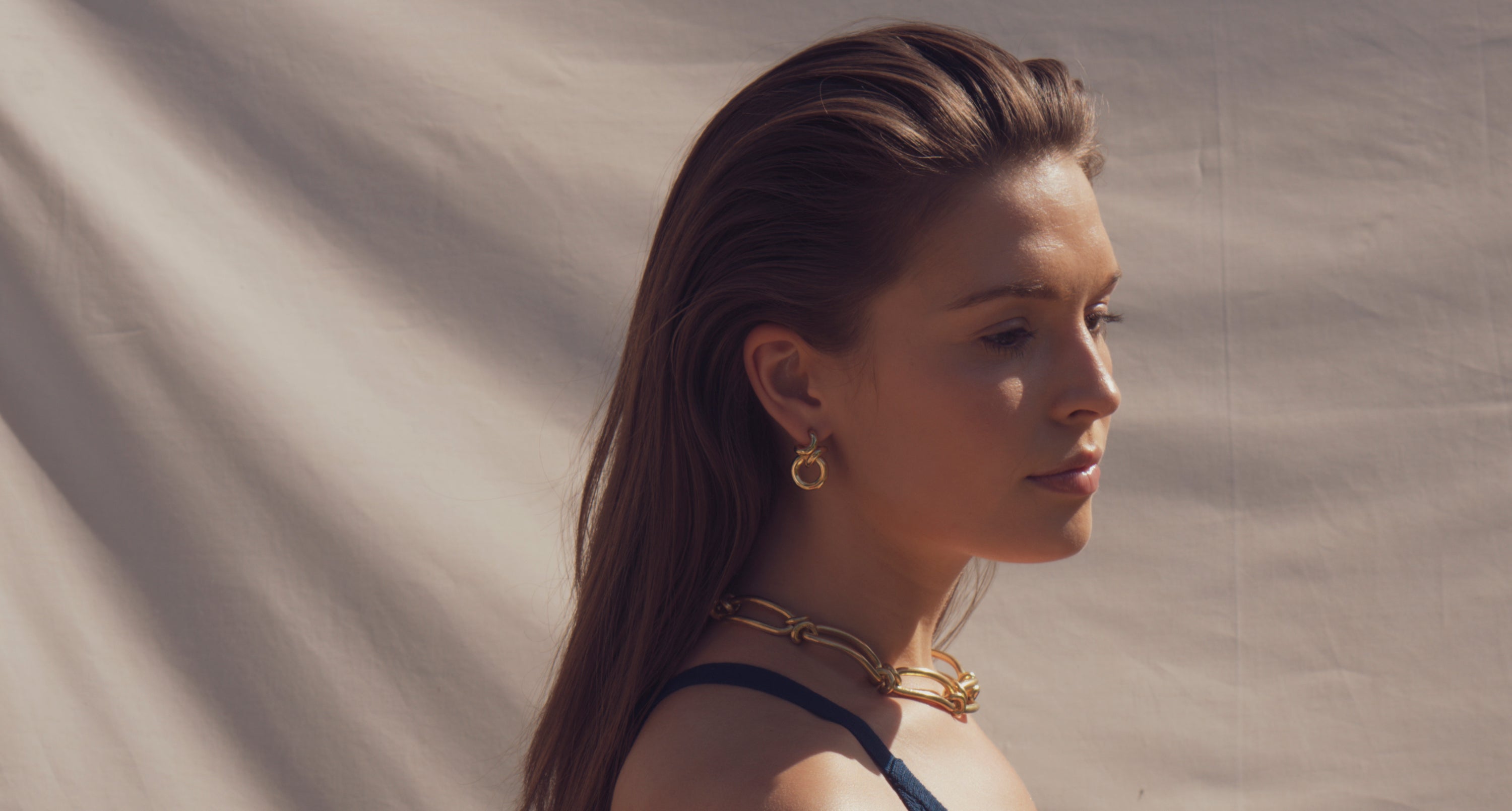 White model against a cream background, facing right, wearing bespoke jewellery by Ruddock Jewellery