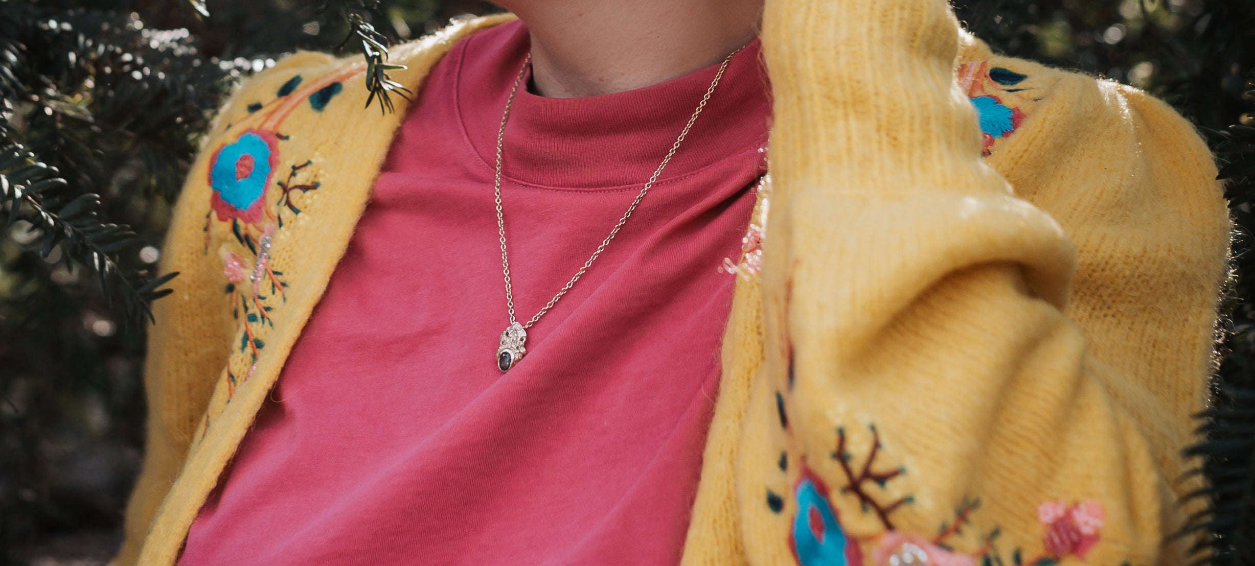 Woman wearing a pink tshirt and yellow cardigan, and a handmade gold necklace by independent jeweller Issy White