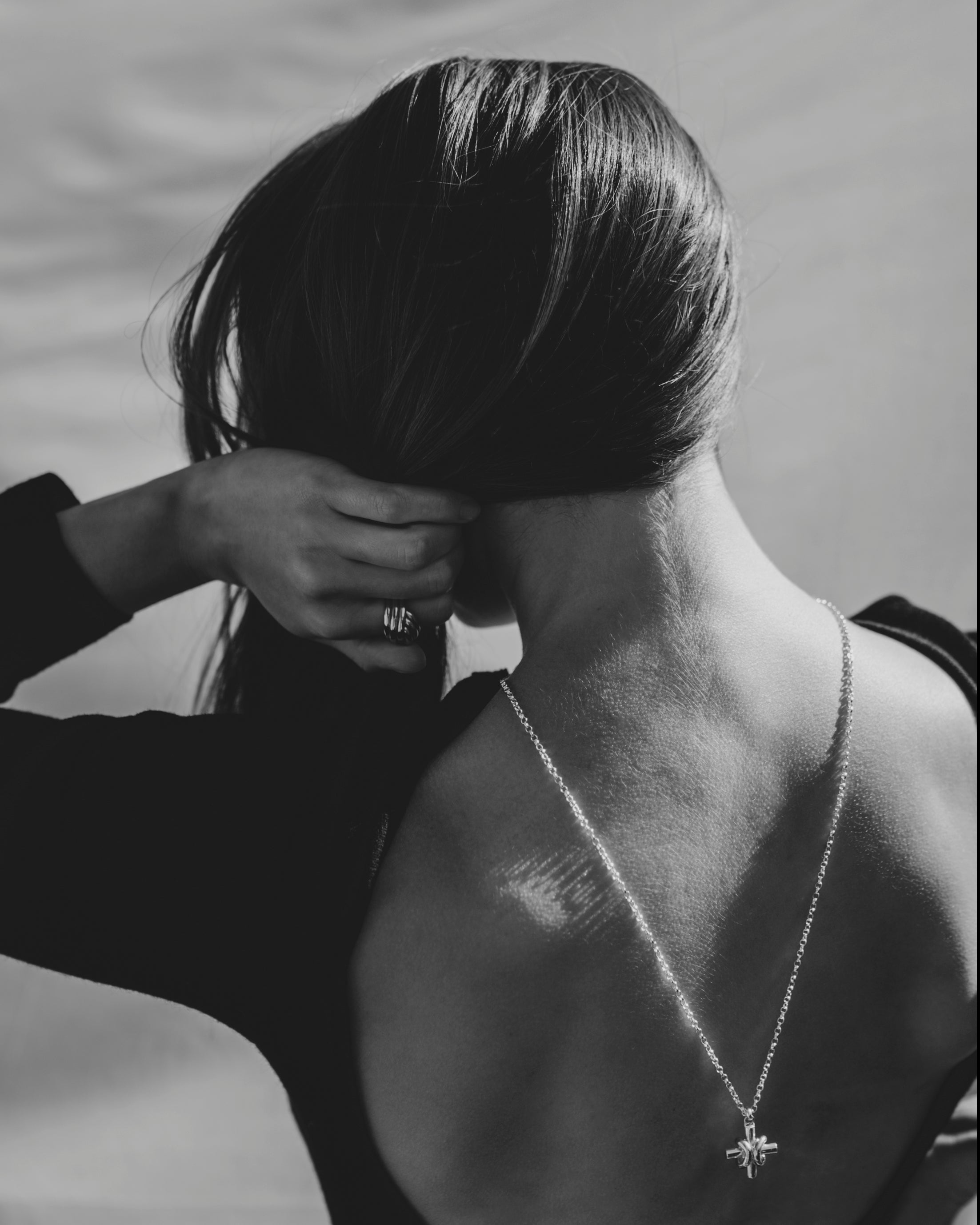 Black and white photo of a female model with her back to the camera, wearing bespoke necklace and bespoke ring by Ruddock Jewellery
