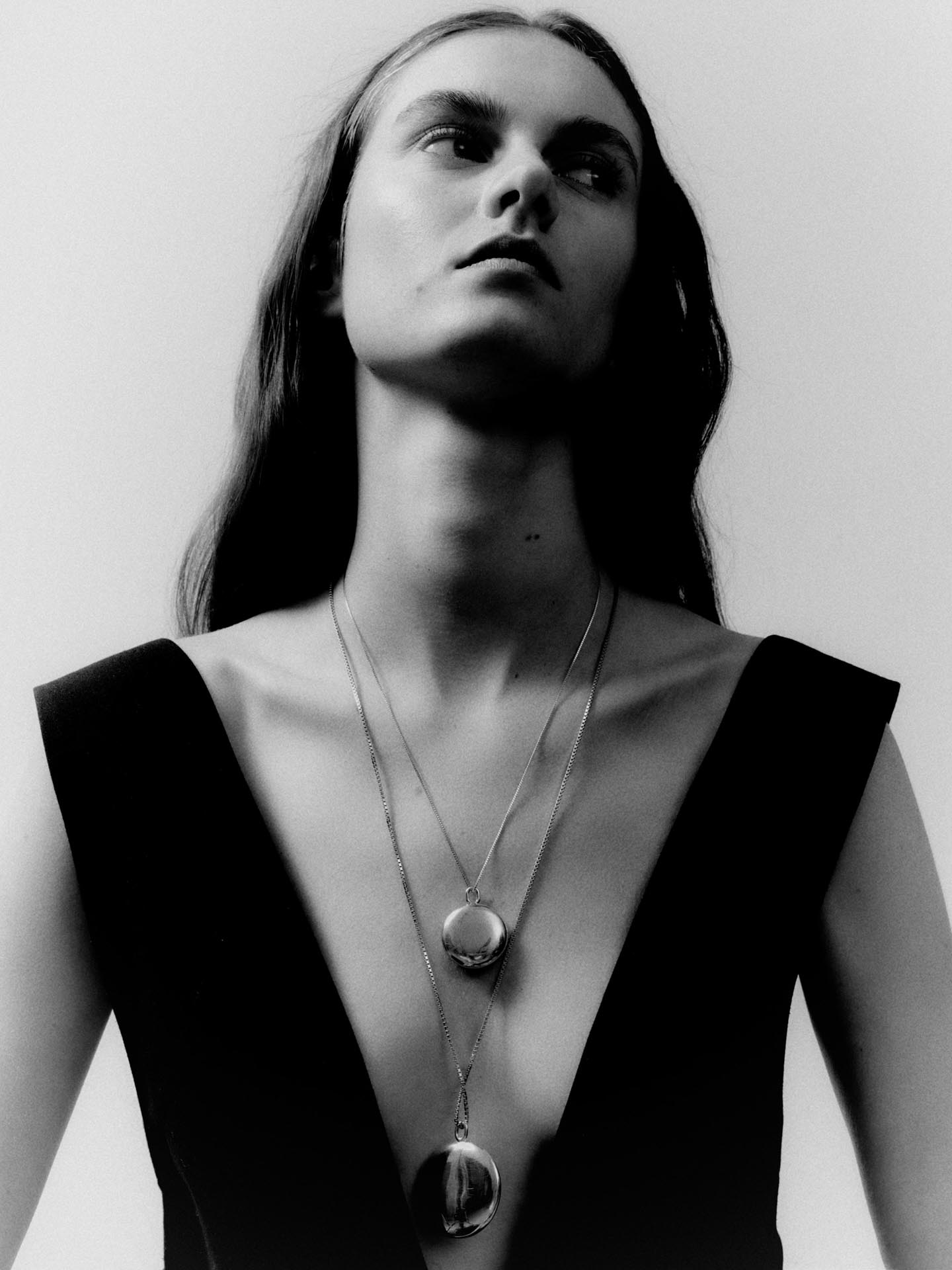 Black and white photo of a model wearing two pendant neck;laces by independent designer Deve
