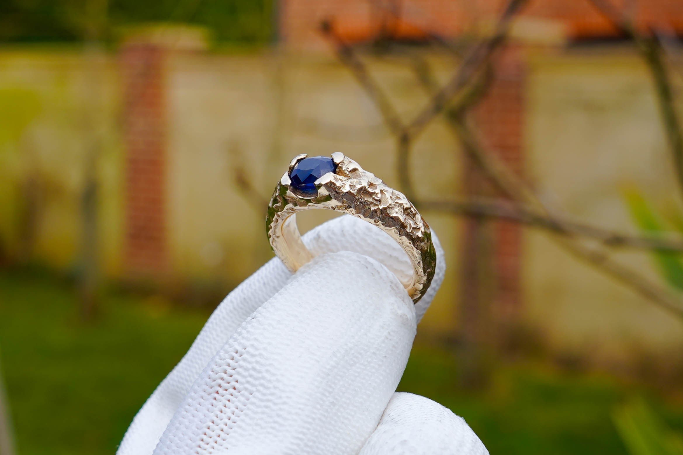 Hand in a white glove holding a bespoke sapphire ring made by Independent jeweller Luke Brient