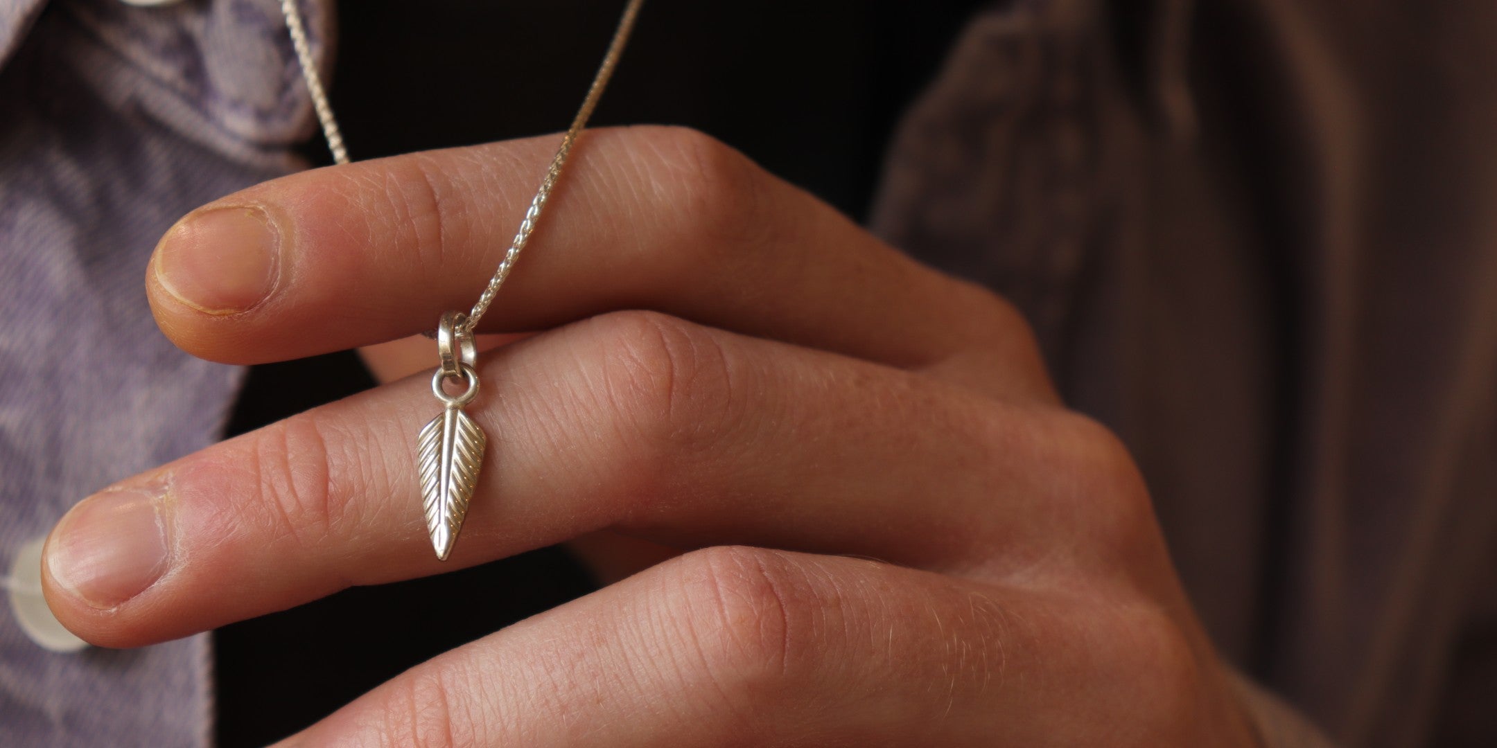 Close up of a man holding a bespoke feather necklace between his fingers 