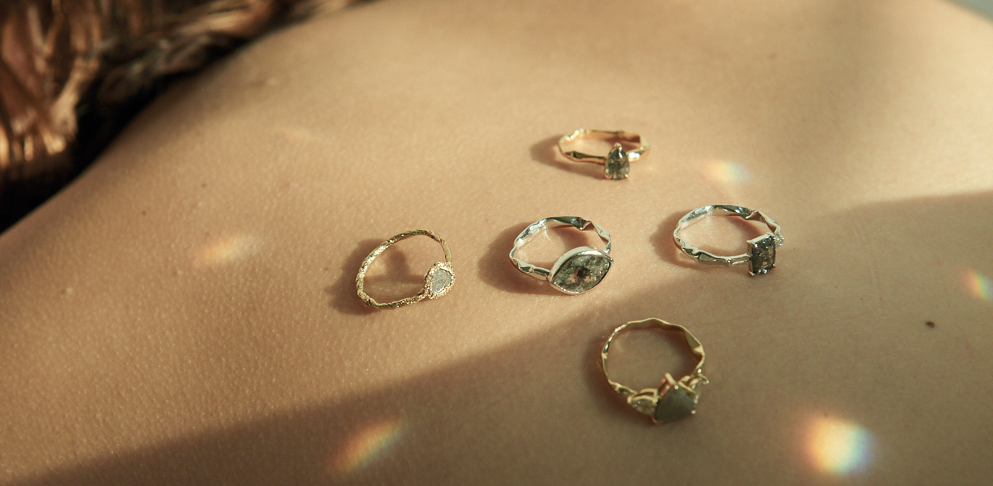 Five bespoke handmade engagement rings against a sandy backdrop