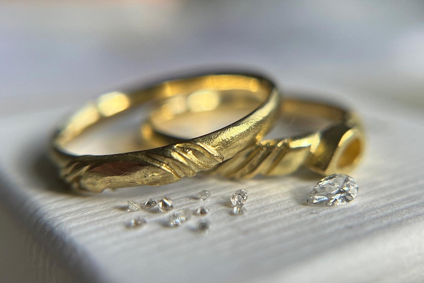Two handmade gold wedding rings next to loose diamonds