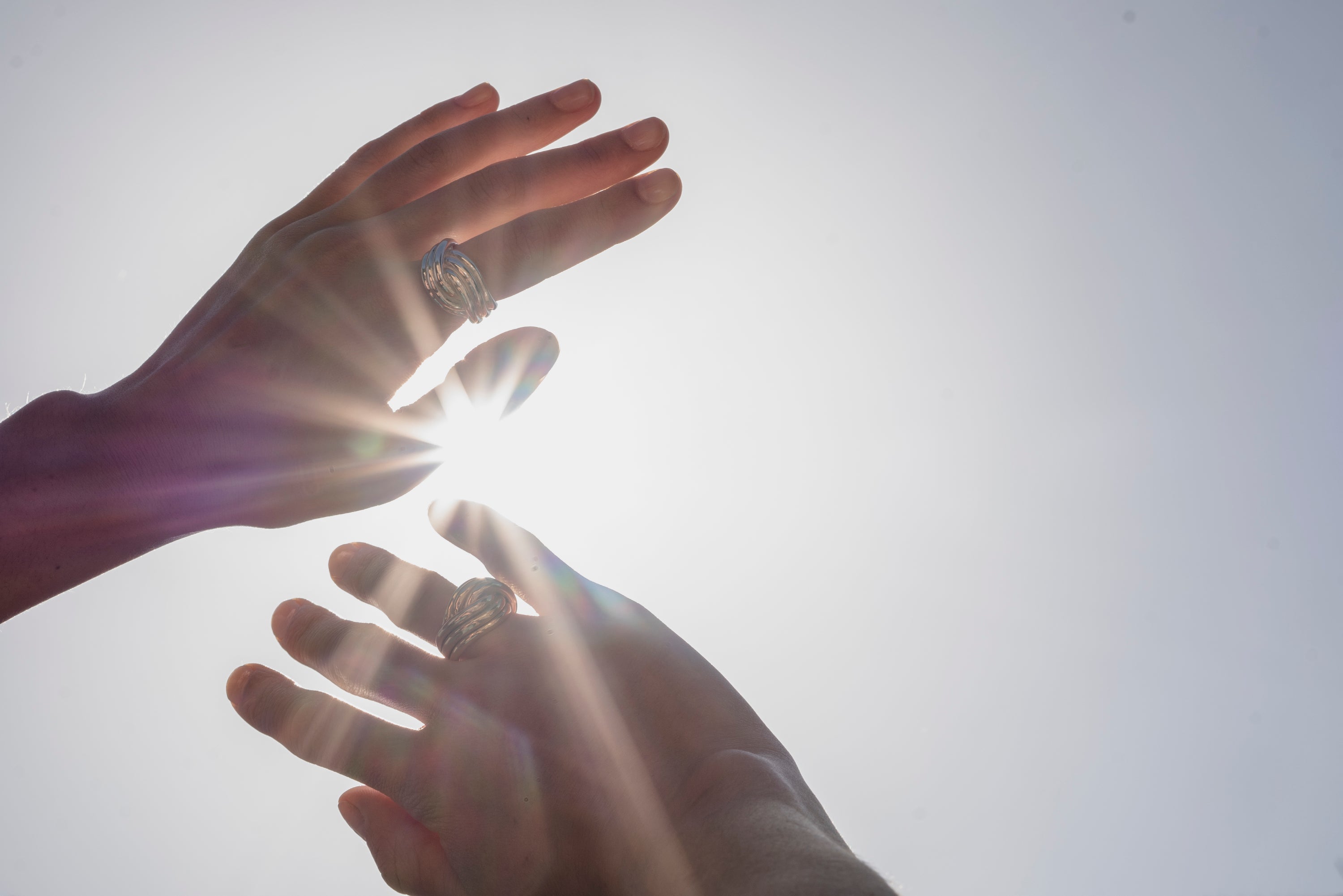 Two hands held in front of the sun, wearing bespoke rings by Ruddock jewellery