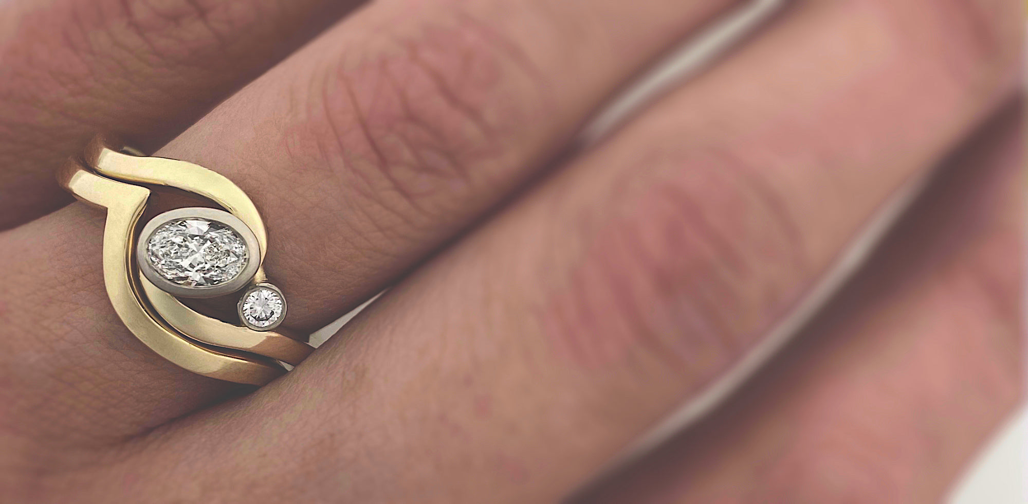 A handmade bespoke gold ring with two diamonds, worn on a hand