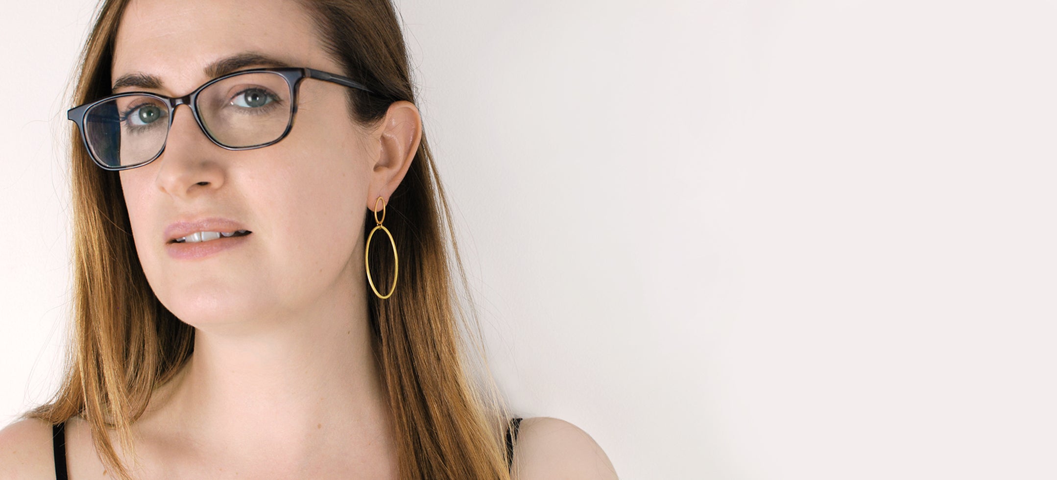 White woman wearing glasses and a handmade gold hoop earring