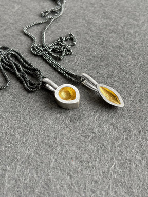 Silver seed pod shaped pendants with oxidised chains on a grey background