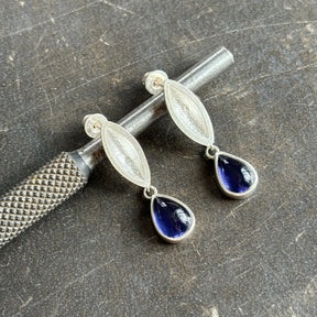 sterling silver sand cast earrings wth iolite stone leaning on a steel tool